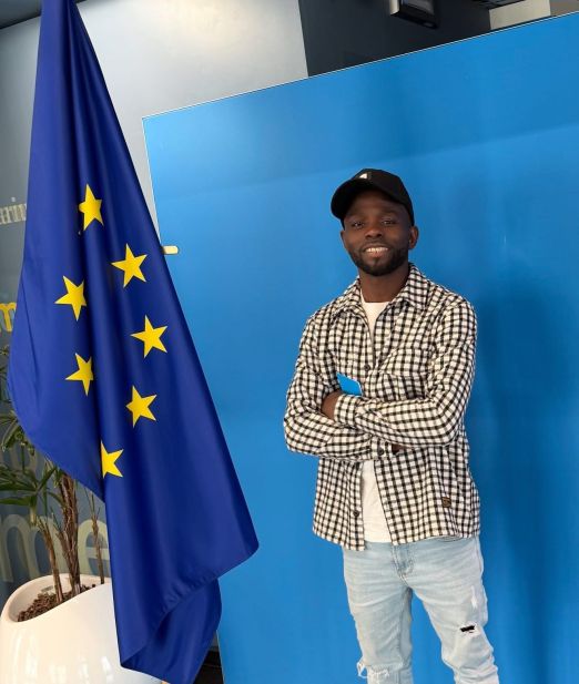 Professional studio portrait, bust (head and shoulders) of a West African man, smart casual (dark blazer, plain shirt, no tie), subtle smile, clean grooming, even soft lighting with slight edge light, seamless navy backdrop color #0B1F3B, high-resolution, realistic photo, corporate branding style